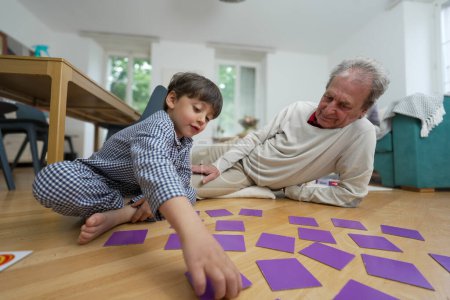 Téléchargez les photos : Young boy and elderly man playing a memory card game, enjoying a fun and engaging activity together, indoor scene with natural light, showcasing intergenerational bonding and family connection - en image libre de droit
