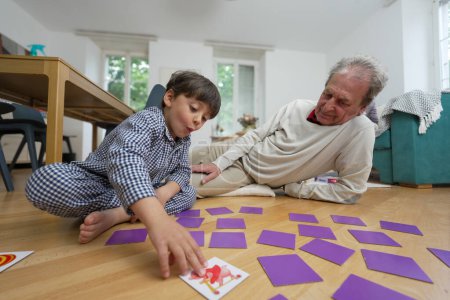 Elderly man and young boy playing a memory game on the floor, engaging in a fun and educational activity, indoor setting with bright light, highlighting intergenerational bonding and family time