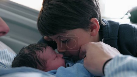 Momento familiar conmovedor - Niño joven dando un beso esquimal al hermano recién nacido en el hospital, hermanos que se reúnen por primera vez después del parto, auténtico momento de cuidado de la vida real