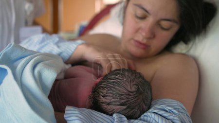 Mother breastfeeds newborn baby for the first time at hospital clinic, authentic real life mom feeding her infant in the first minutes of life, maternal care and growth