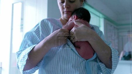 Mutter hält Neugeborenes in der Nähe, in ein gestreiftes Krankenhauskleid gehüllt, unterstreicht die zarte und schützende Bindung, betont die frühe Mutterschaft und die nährenden Momente in einer heiteren Umgebung