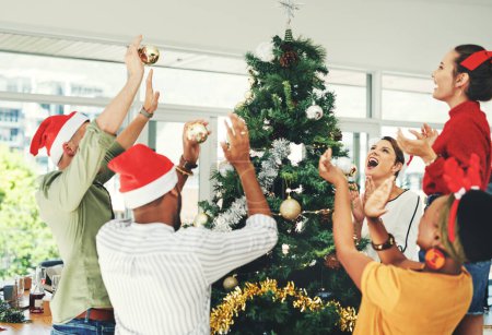 Téléchargez les photos : Cet arbre mérite nos applaudissements. un groupe de jeunes hommes d'affaires décorant ensemble un sapin de Noël au travail - en image libre de droit