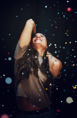 Feeling the rhythm of the music. an attractive young woman dancing alone against a dark background at a New Years party