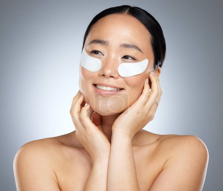 Beauty, skincare and woman using eye patch, face mask or dermatology product against mockup studio background. Happy asian girl model using facial cosmetics on skin for a healthy glow with collagen.