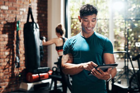 Photo for Thank God for modern fitness apps. a handsome young sportsman using a digital tablet in a gym with his fitness partner in the background - Royalty Free Image
