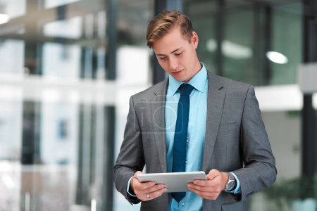 Foto de Mantenerme por encima de mis tareas. un joven hombre de negocios guapo parado solo en su oficina y usando una tableta - Imagen libre de derechos