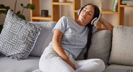 Détendez-vous, musique et paix avec la femme sur le canapé avec écouteurs pour dormir, podcast ou bien-être. Technologie, streaming et service avec fille dans le salon à l'écoute pour le calme, spirituel et style de vie.