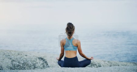 Photo for I am at peace with myself. Rearview shot of an unrecognizable woman sitting cross legged and meditating alone by the ocean during an overcast day - Royalty Free Image