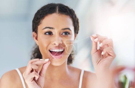 Téléchargez les photos : Quand vous nettoyez, faites-le correctement. une jeune femme séduisante en soie dentaire dans la salle de bain à la maison - en image libre de droit