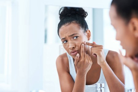 Photo for I cant go out with this. a beautiful young woman squeezing a pimple in the mirror - Royalty Free Image