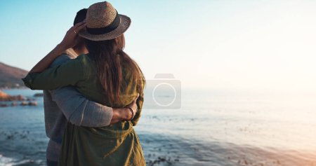 Foto de Los días de verano son para la playa y bae. Vista trasera de una pareja joven y cariñosa abrazándose en la playa al atardecer - Imagen libre de derechos