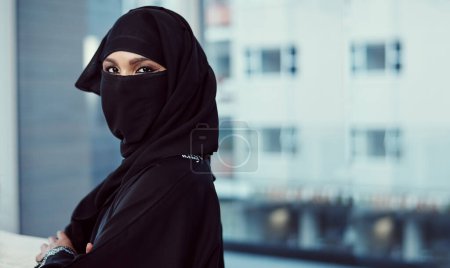 Foto de Estoy haciendo de este lugar de trabajo mío. Retrato recortado de una mujer de negocios árabe en un burka de pie en su oficina - Imagen libre de derechos