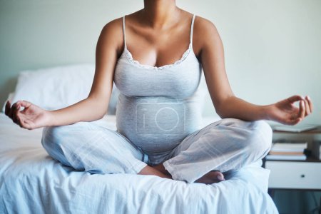 Téléchargez les photos : Vous avez besoin de toute la paix que vous pouvez obtenir pendant la grossesse. une femme enceinte méconnaissable pratiquant le yoga dans sa chambre à coucher à la maison - en image libre de droit