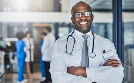 Photo for Keeping you healthy keeps me happy. Portrait of a confident doctor working in a hospital with his colleagues in the background - Royalty Free Image