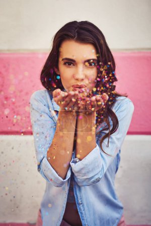 Adding colour to your life. Portrait of a beautiful young woman blowing confetti outside
