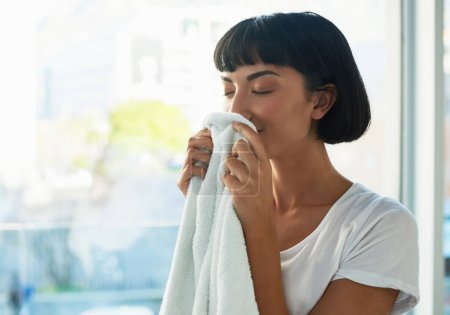 Téléchargez les photos : Cette odeur fraîche de lessive en vaut la peine. une jeune femme sentant les serviettes fraîchement lavées à la maison - en image libre de droit