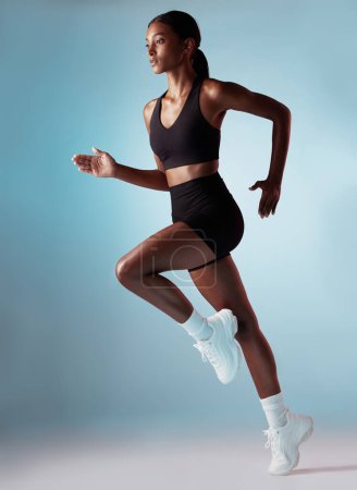 Téléchargez les photos : Fitness, santé et femme noire en cours d'exécution en studio avec fond bleu. Sport, exercice et forme, motivation pour un entraînement cardio coureur fort pour un marathon ou une course, entraînement pour une femme jamaïcaine - en image libre de droit