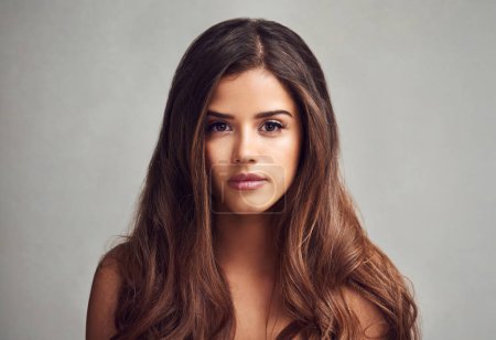 Her beautiful hair will bewitch you. Studio shot of a young beautiful woman with long gorgeous hair posing against a grey background