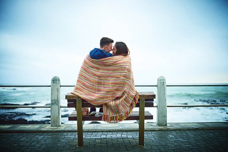 Foto de El amor los mantendrá calientes. una feliz pareja joven cubriéndose con una manta al aire libre - Imagen libre de derechos