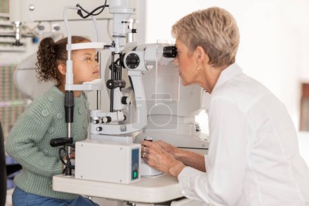 Optiker bei einem Sehtest an Mädchen in einem Optiker-, Brillen- und Optikergeschäft mit Autorefraktor. Augenpflege, Ausrüstung und Kind erhalten Augenuntersuchung von einem leitenden medizinischen Optiker in einer optischen Klinik.