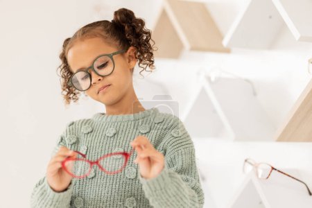 Glasses, options and children with a girl in an optometry store while shopping for prescription lenses. Kids, retail and vision with a female child customer looking at eyewear at the optometrist.