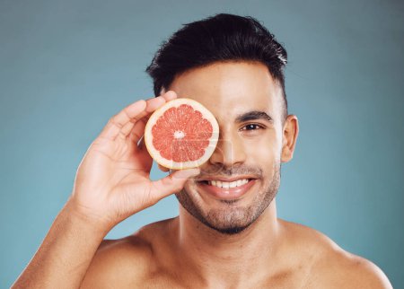 Grapefruit, man and skincare in studio for vitamin c, healthy wellness and natural glow on blue background. Portrait of happy guy model face, nutrition and body detox for cleaning beauty cosmetics.