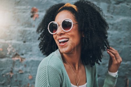 Fashion, summer and black woman in city with beauty, sunglasses and smile by blue brick wall. Travel, adventure and girl with trendy outfit having fun on weekend, holiday and vacation in urban town.