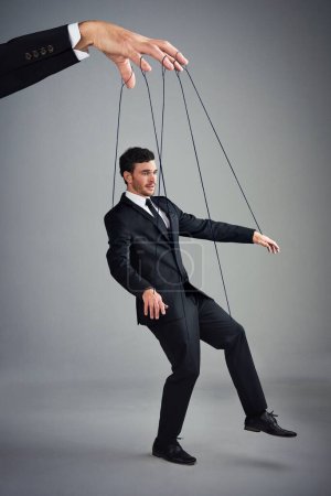 Photo for If you dont control your business, someone else will. Studio shot of a young businessman being controlled like a puppet by a giant hand against a gray background - Royalty Free Image