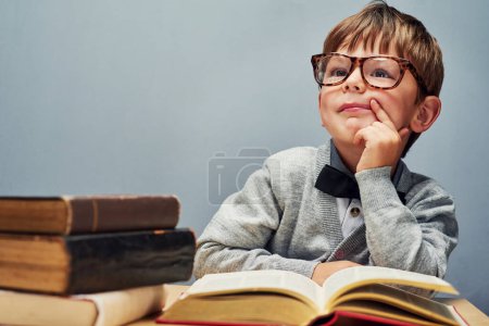Den Neugierigen gehört die Zukunft. Studioaufnahme eines smarten kleinen Jungen, der Bücher liest und nachdenklich vor grauem Hintergrund wirkt