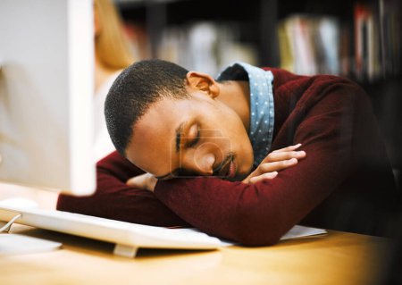 Téléchargez les photos : Il travaille dur toute la semaine. un jeune homme fatigué dormant sur un bureau les bras croisés à l'intérieur d'une bibliothèque - en image libre de droit
