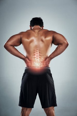 Photo for Injuries are just a part of the package. Rearview shot of a sporty young man holding his back in pain against a grey background - Royalty Free Image