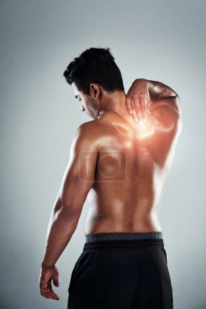 Photo for Hes tweaked something in his back. Rearview shot of a sporty young man holding his back in pain against a grey background - Royalty Free Image