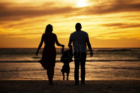 Photo for Silhouette, beach and family at the sea at sunset, holding hands and playing, bonding and relax together. Shadow, happy family and child with parents at sunrise, travel, freedom and love in Bali. - Royalty Free Image