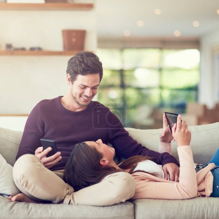 Photo for Time together is time well spend. a smiling young couple using digital tablets while relaxing together on the sofa at home - Royalty Free Image