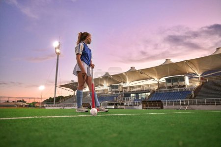 Photo for Hockey, stadium and woman sports training, thinking of game strategy and goal fitness health on green pitch field with sunset sky. Young teenager or athlete girl with training gear for competition. - Royalty Free Image