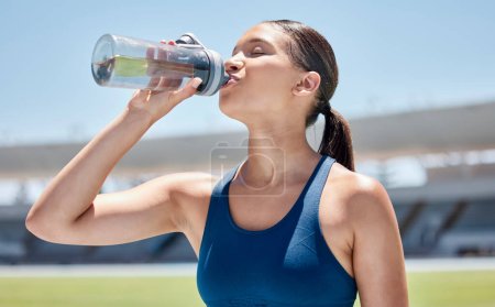 Photo for Drinking water, sports and woman athlete on an outdoor exercise field for training and fitness. Wellness, women workout and person thirsty in the sun relax after a runner challenge with a bottle. - Royalty Free Image