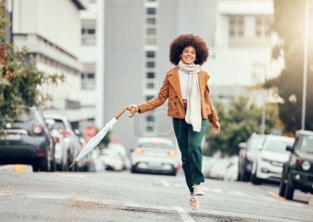 Photo for Black woman, umbrella and jump on street, city or road outdoors. Happy, smile and carefree female from South Africa skipping on pavement in urban town, traveling or having fun time alone on sunny day. - Royalty Free Image