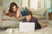 What are you looking at, honey. a happy young couple relaxing on the sofa at home Poster #620511946