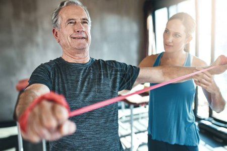 Exercise is vital for healthy aging. a senior man using resistance bands with the help of a physical therapist