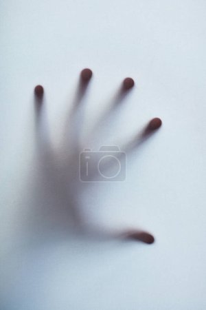 Feeling trapped. Defocussed shot of a single hand reaching out against a plain background