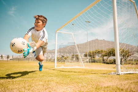 Football, boy goalkeeper and jump, saving ball from goals at outdoor sports field. Soccer, kid and competition game with fitness, goal keeper and soccer ball on grass, success and action to save goal.