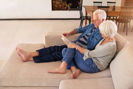 Foto de Y vivieron y amaron felices para siempre. una pareja de ancianos relajados leyendo un libro juntos en el sofá en casa - Imagen libre de derechos