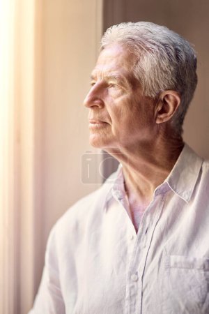 Reminded of the past, but not defined by the past. a thoughtful senior man looking out of the window at home Poster 621234326