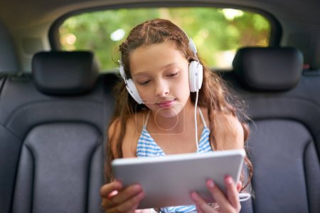 Foto de Mantener el viaje en coche entretenido. una joven sentada en un coche con auriculares y una tableta digital - Imagen libre de derechos