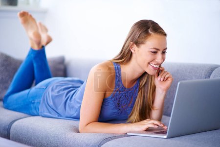 Téléchargez les photos : Quel super blog. une jeune femme utilisant son ordinateur portable sur le canapé à la maison - en image libre de droit