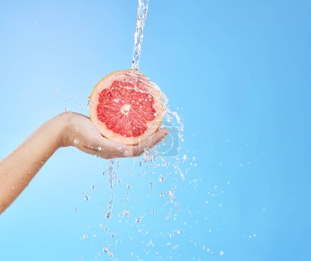 Hand, grapefruit and water splash for skincare nutrition, wellness or cosmetics against a blue studio background. Person hold citrus fruit in healthy, hydration or hygiene for natural vitamin C skin.