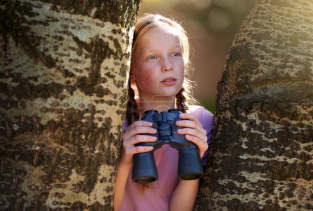 Téléchargez les photos : L'aventure est là-bas. une petite fille avec une paire de jumelles en plein air - en image libre de droit