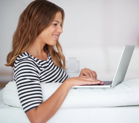 Staying connected is just so easy. a young woman using a laptop while sitting on a sofa at home Poster 623844716