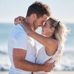 Couple, love and hug at the beach together, nose touch and bonding with travel and date by the ocean for summer holiday. Happy, man and woman with quality time, sea waves and romantic out in nature