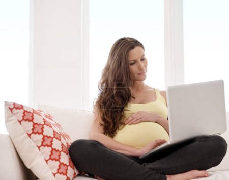 Buscando algunos consejos de nacimiento. una joven embarazada que trabaja en su ordenador portátil en casa
